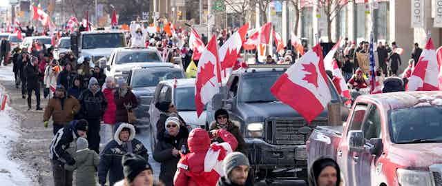 A line of trucks and supporters parade down Bloor Street in Toronto. There are over 20 Canadian Flags visible.