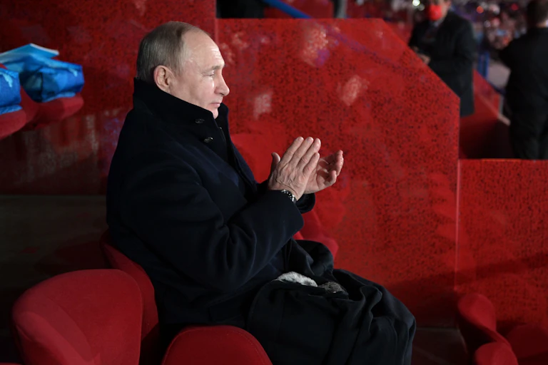 A man is clapping his hands as he sits alone in a red chair.
