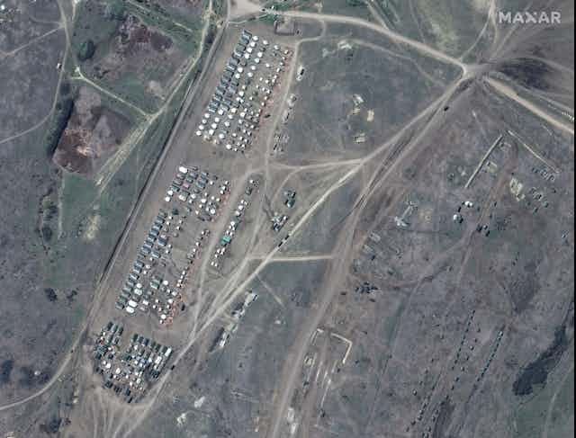 Satellite view of green and brown terrain, roads and numerous white and green rectangles arranged in orderly rows