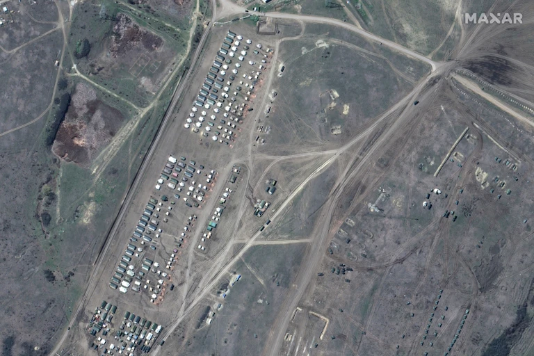 Satellite view of green and brown terrain, roads and numerous white and green rectangles arranged in orderly rows