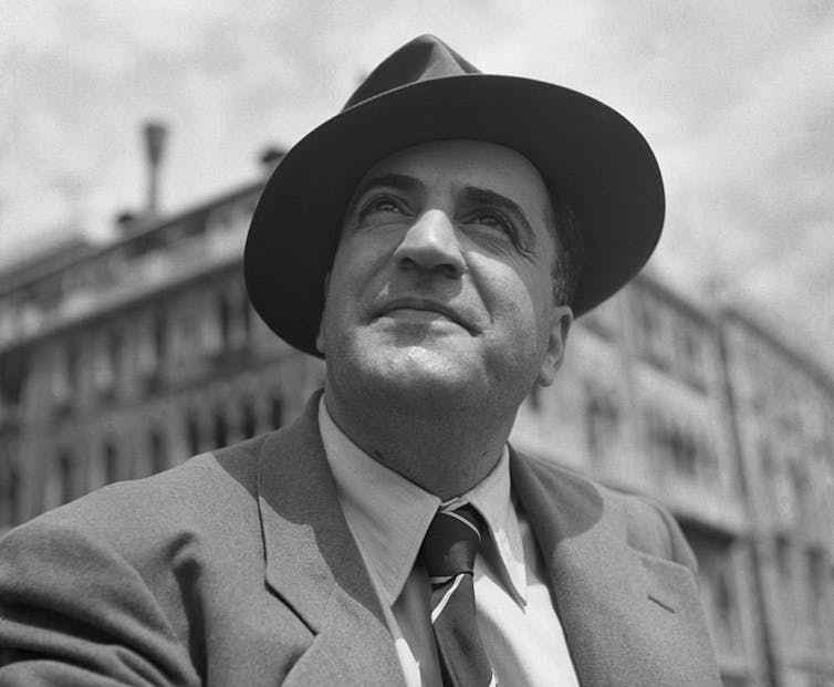 A man in a hat and suit looks toward the sky.
