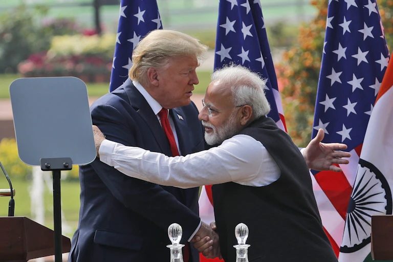 Modi embraces Trump. Behind them, stand three American flags.