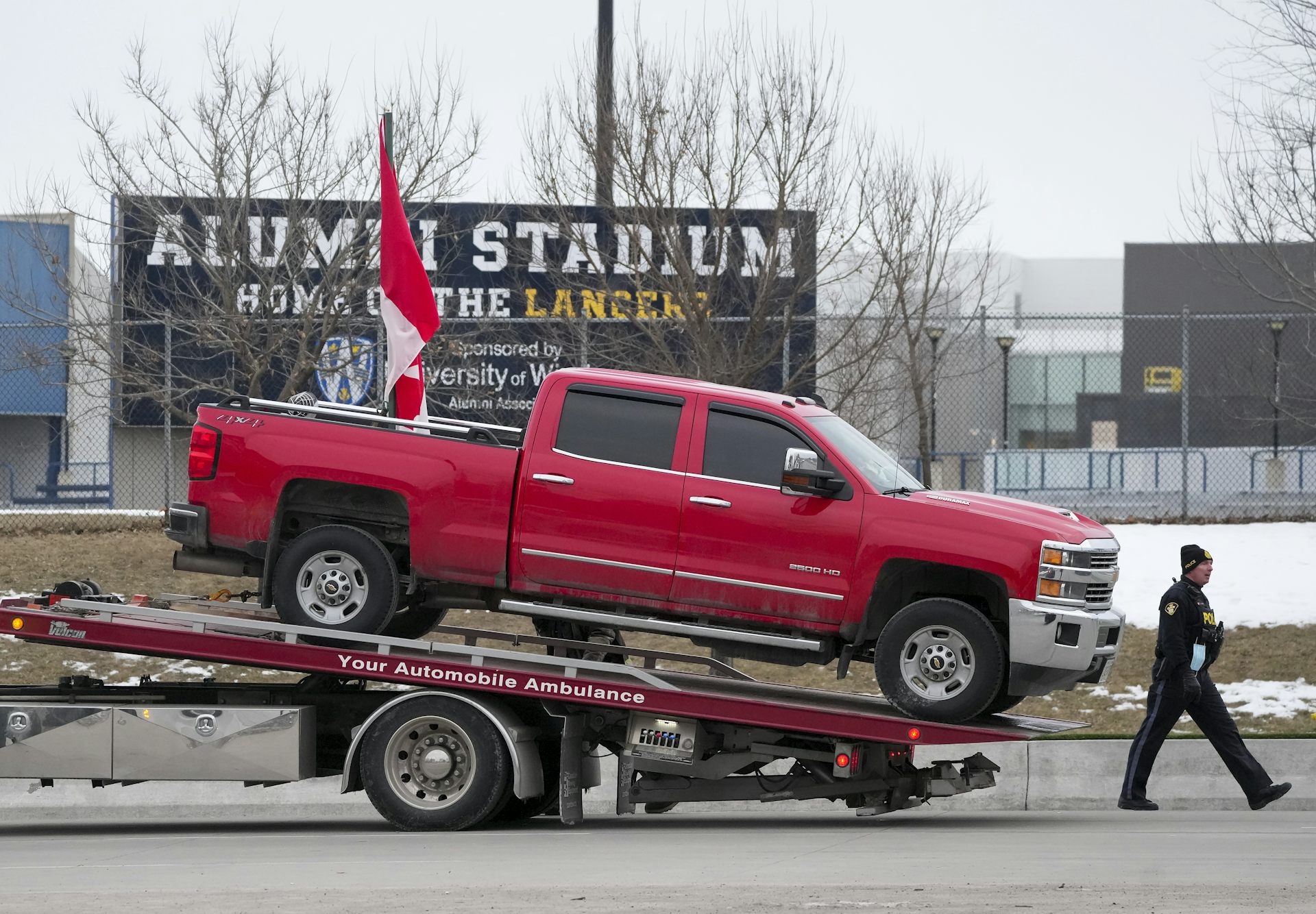 Police tow a red pickup truck with a Canadian flag in its cab.