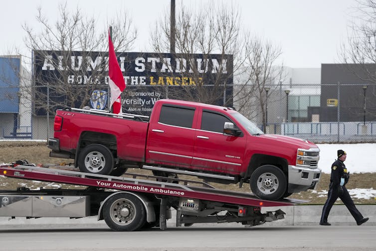 Police tow a red pickup truck with a Canadian flag in its cab.