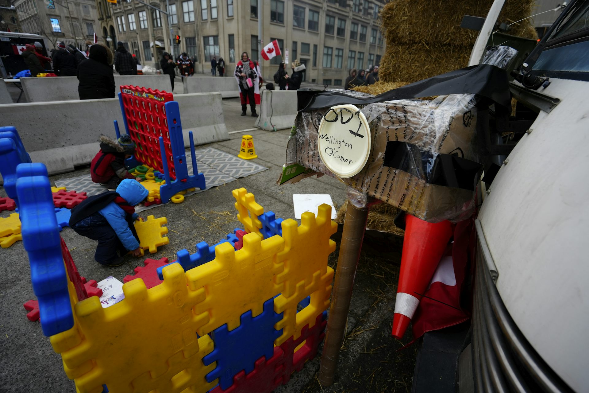 Children in snowsuits seen playing with large snap together colourful blocks beside a truck on the street.