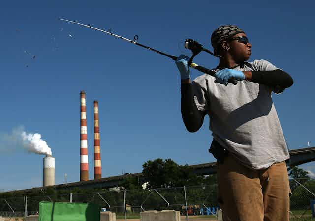 A woman fishes with a power plant in the background.
