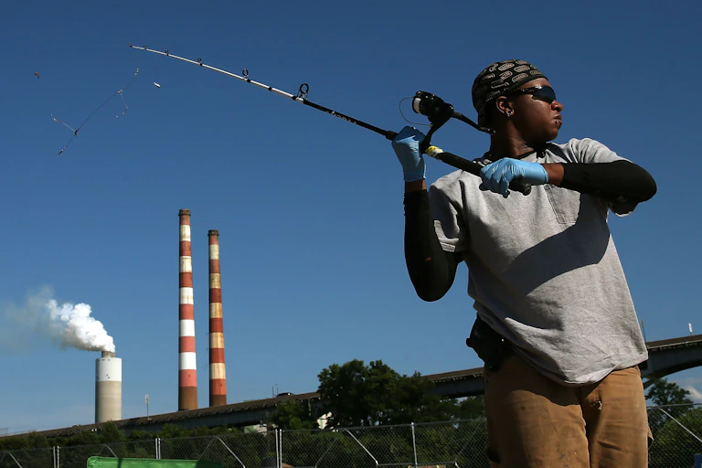 A woman fishes with a power plant in the background.