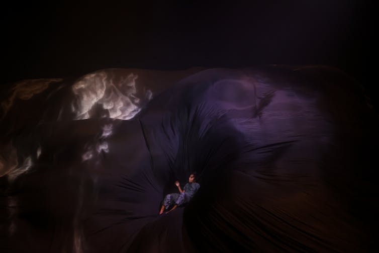 A dancer enveloped by a giant sheet of silk.