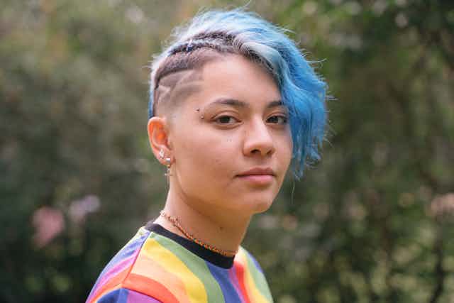 Gender diverse young person wears a rainbow top and blue hair.