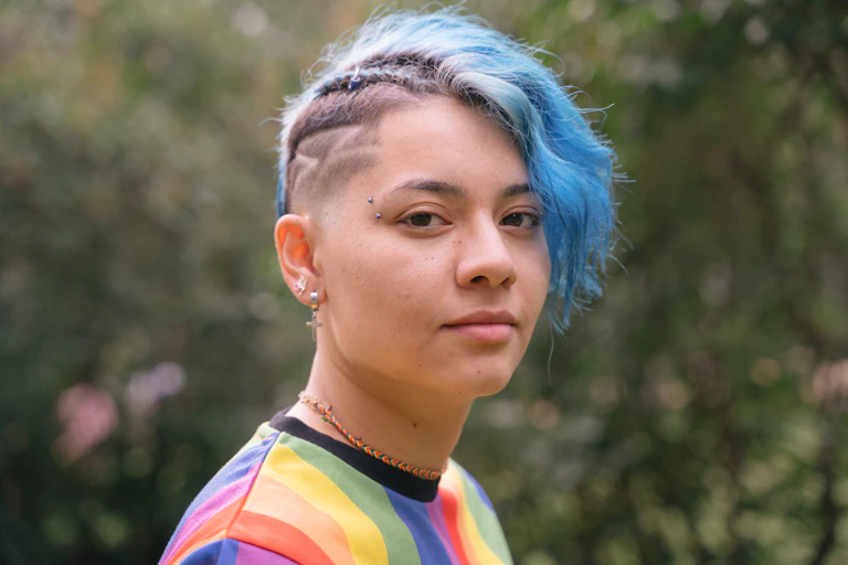 Gender diverse young person wears a rainbow top and blue hair.