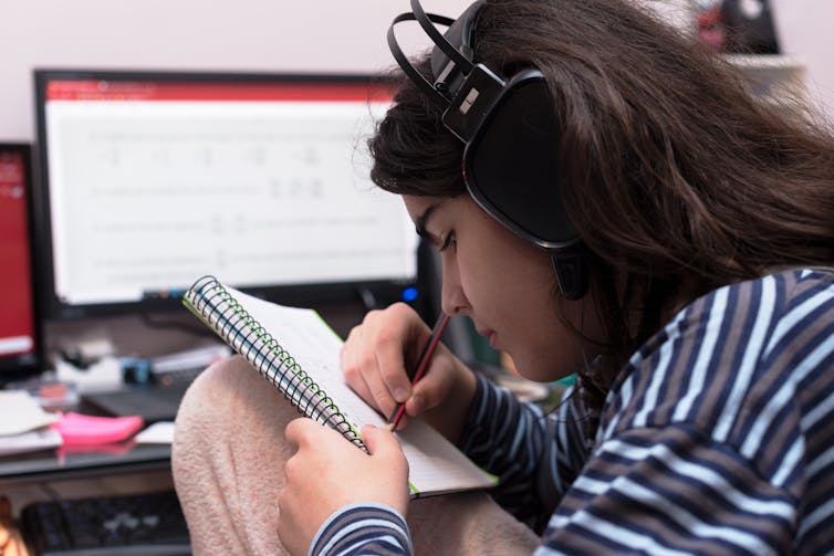 Young trans person writes on a notepad, while listening to music.