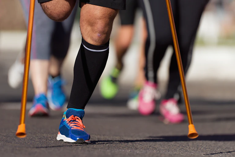 Gros plans du bas du corps d'un marathonien, amputé de la jambe droite (et appuyé sur ses béquilles)