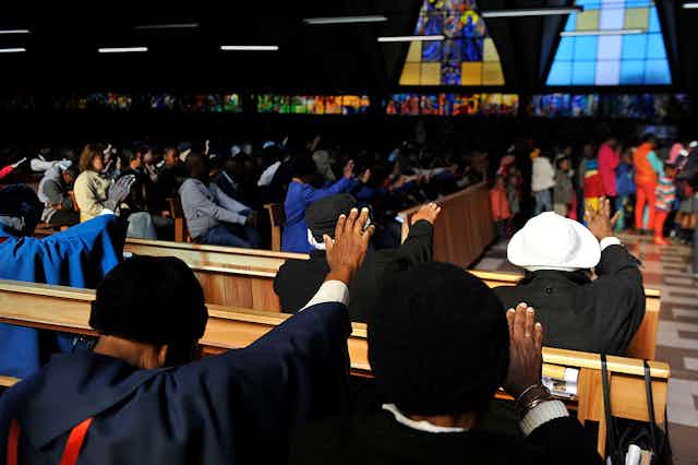 women in a church service, with their hands stretched out. 