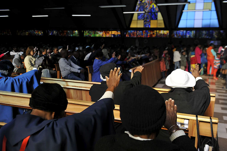 women in a church service, with their hands stretched out.