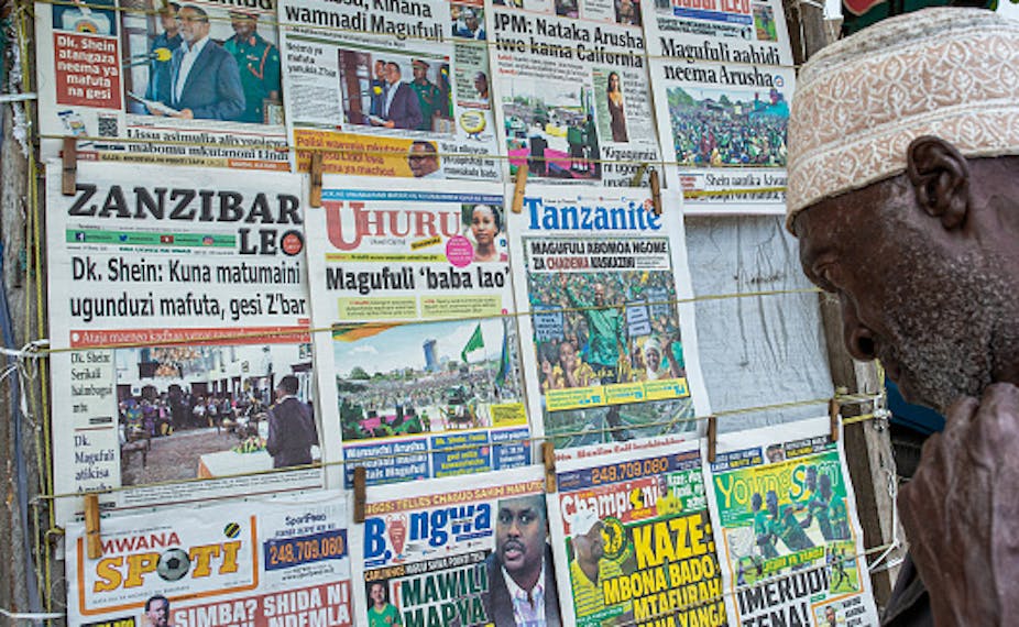An elderly man wearing a cap looks intensly at front pages of newspaper at a kiosk in Zanzibar