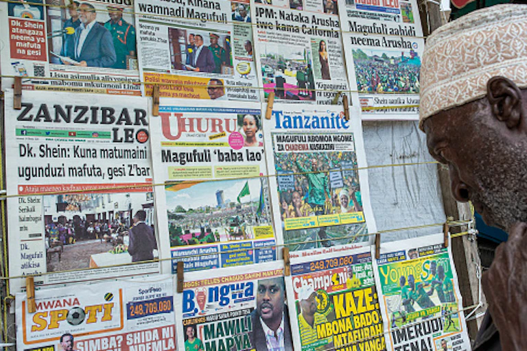 An elderly man wearing a cap looks intensly at front pages of newspaper at a kiosk in Zanzibar