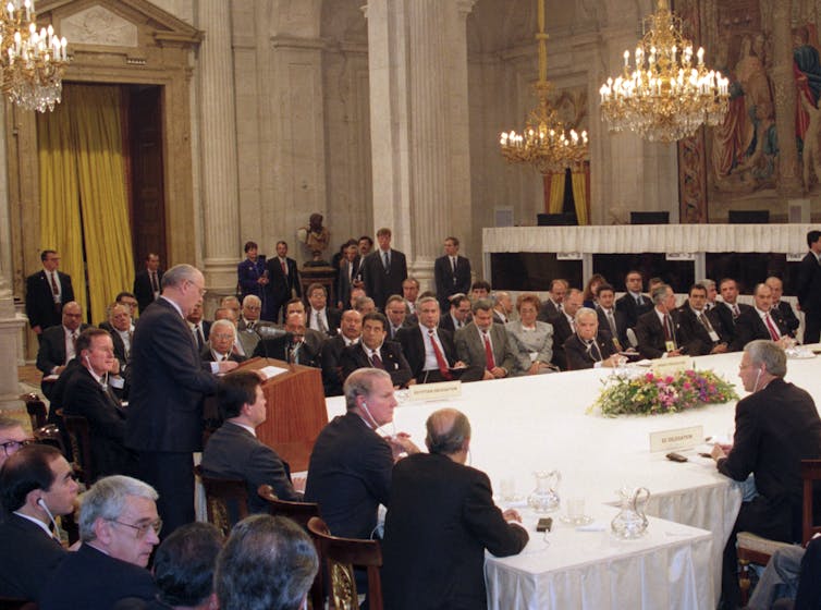Mikhail Gorbachev stands at a lectern speaking to a room of world leaders.