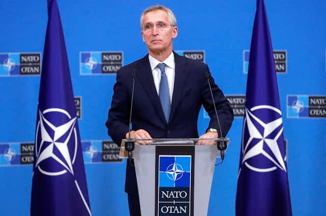 Nato secretary-general Jans Stoltenberg stands at a podium flanked by Nato flags.