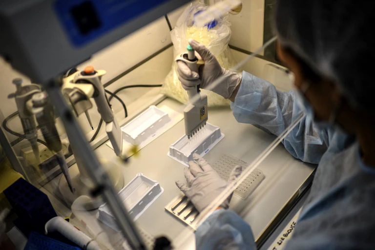 Le spécialiste, en tenue de protection, effectue une manipulation sur les prélèvements à analyser.