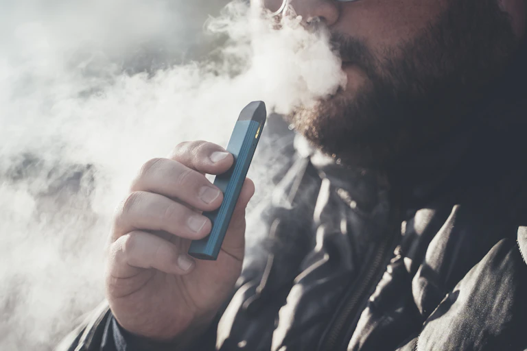 Un hombre con un cigarrillo electrónico que le cubre la cara de humo.