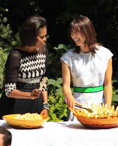 Michelle Obama and Samantha Cameron serving food at a barbeque.