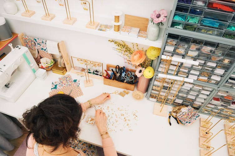 A woman seen from above making earrings at a workbench.