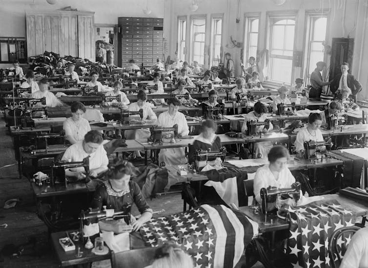 Women sewing American flags in a 1920s naval yard warehouse.