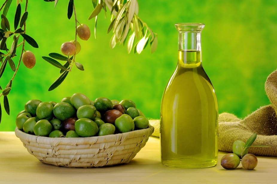 A bottle of extra virgin olive oil next to a basket of olives.