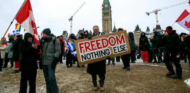 A man holds a sign on parliament hill that reads 'freedom nothing else'