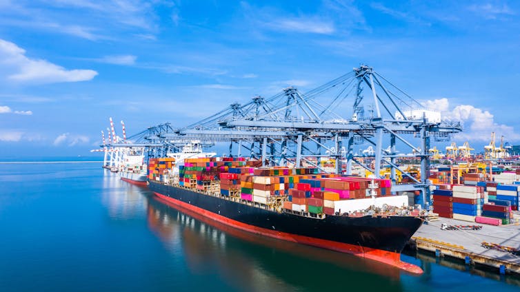 A large vessel laden with colourful containers in a busy harbour.