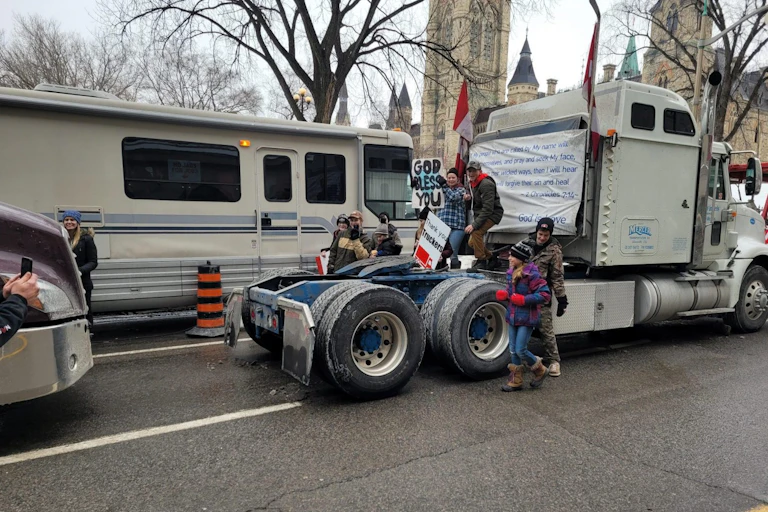 A transport truck with a family posing on the back carrying 'god bless you' signs.