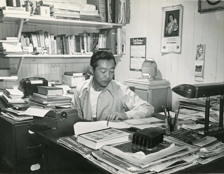 Man sits at desk in front of typewriter.