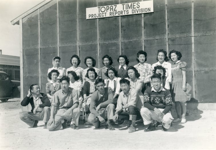 A group of Japanese Americans poses in front of a building at an internment camp.