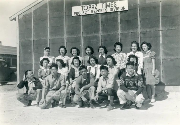 A group of Japanese Americans poses in front of a building at an internment camp.