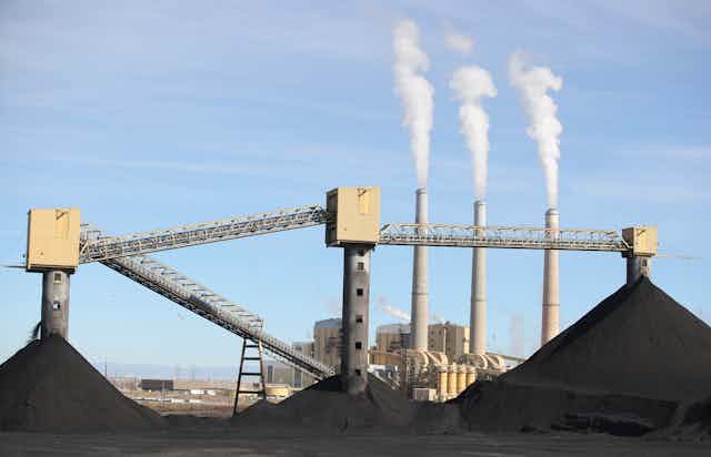 Piles of coal with three tall smokestacks in the bacground