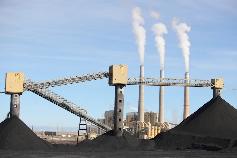 Piles of coal with three tall smokestacks in the bacground