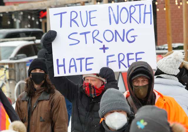 Man holding a sign that says "TRUE NORTH STRONG + HATE FREE"