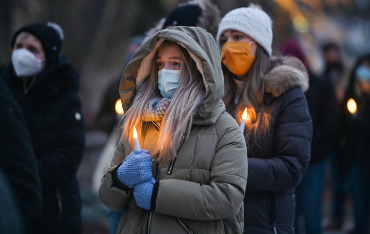 People dressed in coats holding burning candles for a memorial.