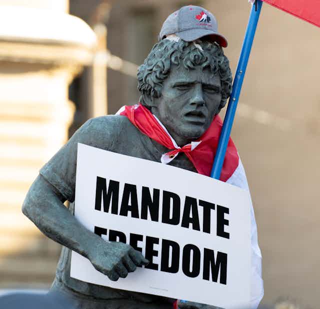 The Terry Fox statue has a Hockey Canada hat on it, as well as a Canadian flag and a sign that says MANDATE FREEDOM.