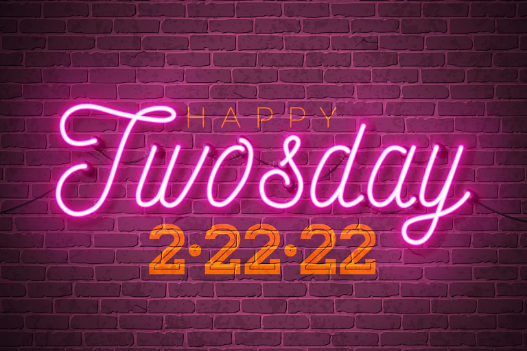 A neon sign against a brick wall reads, "Happy Twosday 2/22/22."