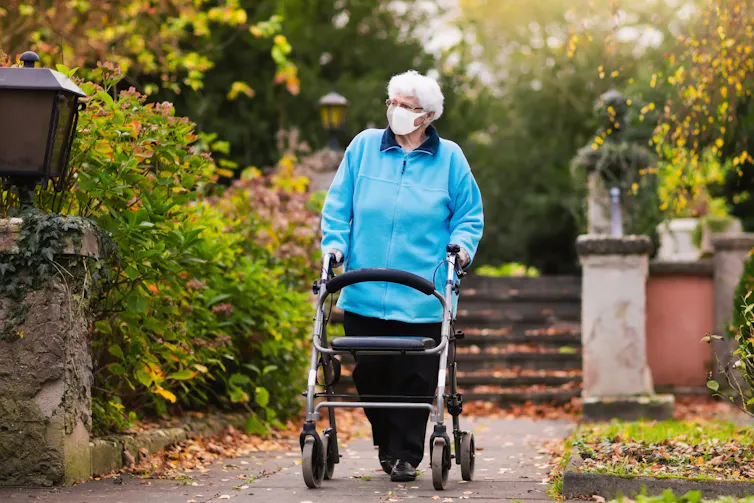 A woman with a walker goes through a garden.