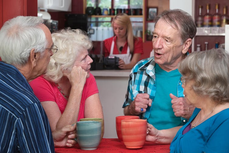A group of older people chat around a table.