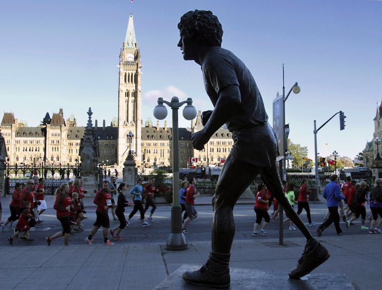 Participants in a running race run by the statue of Terry Fox that is across the street from the Canadian Parliament Buildings.