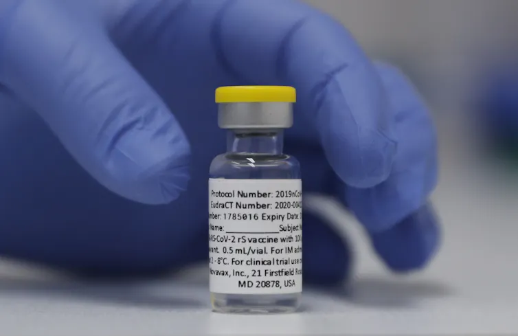 Gloved hand reaches for a Novavax vial.