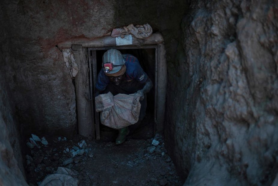 A man emerges from a mining shaft with a bag of gold ore