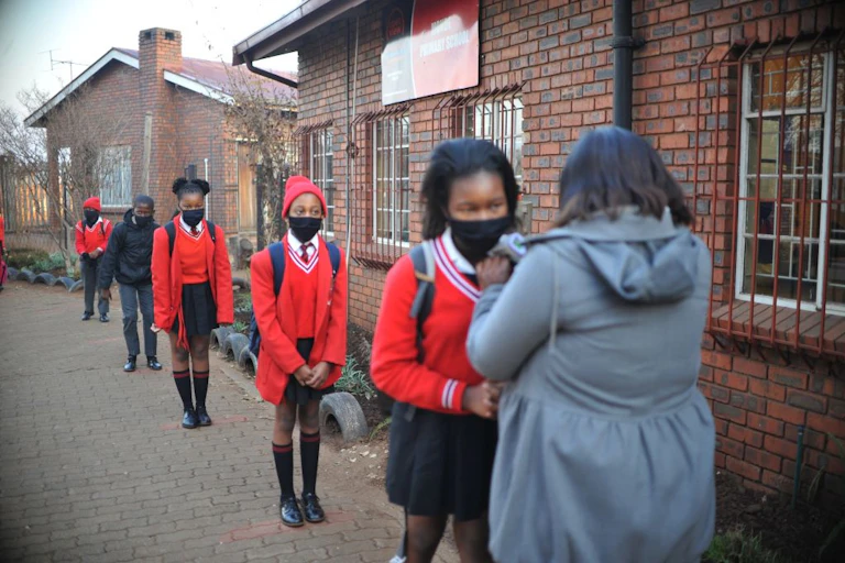School children waiting in a queue to be screened in adherence to COVID-19 protocols by their teachers as they enter the school premises.