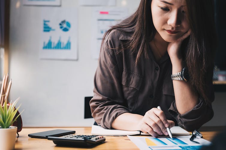 A woman sits at a desk with papers and a calculator.
