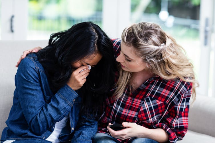 A woman cries on another woman's shoulder.