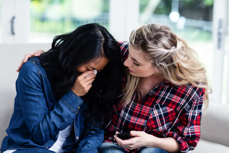 A woman cries on another woman's shoulder.