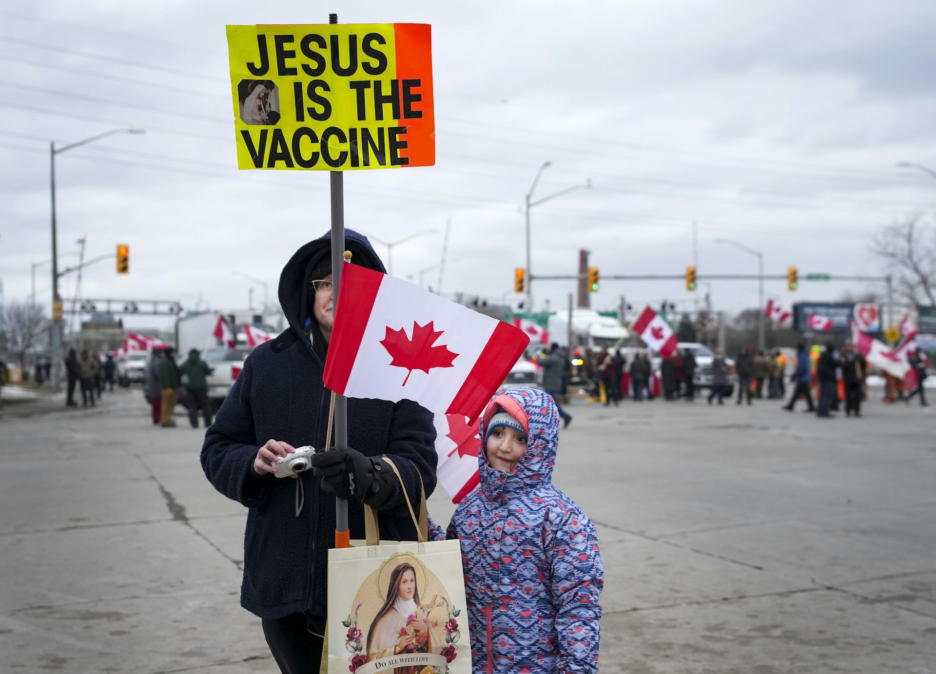 A woman stands with her child holding a sign that reads 'Jesus is the vaccine'
